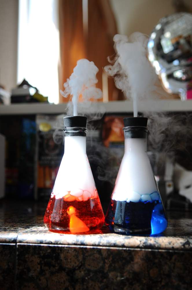 Two science beakers one filled with red liquid and one with blue, steam with dry ice